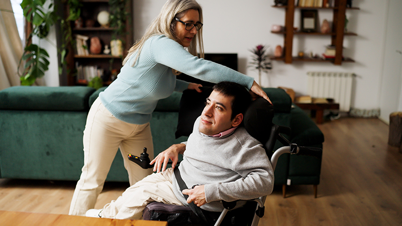 Caregiver supporting man with mobility limitation in modern home